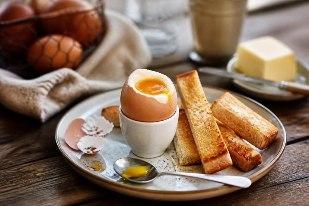 Œuf à la coque parfait servi en coquetier avec des mouillettes dorées, jaune coulant visible, sur une table en bois clair